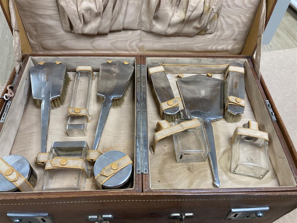 A 1930s Art Deco travelling toilet case, containing eleven silver mounted jars, mirror, and brushes.